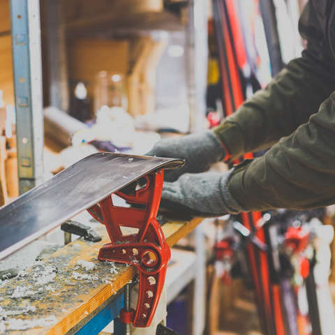 Ein Mann bereitet einen Ski zum Skiwachsen vor indem er ihn auf einer Werkbank einspannt.