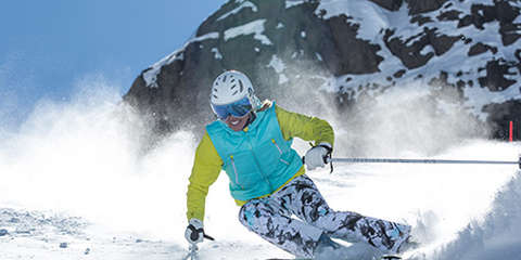 Ein Skifahrer bei der Abfahrt auf der Piste. Er trägt einen weißen Alpina Skihelm und eine Alpina Skibrille mit Airframe Venting Technologie.