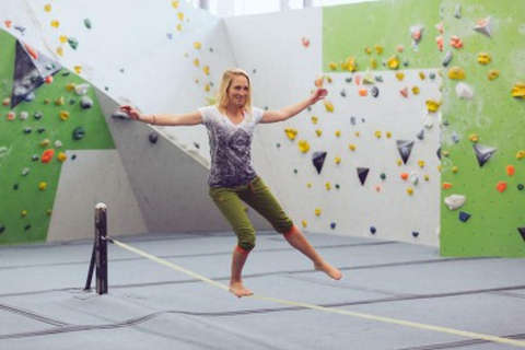 Eine Frau trainiert ihre Balance auf einer Slackline in einer Boulderhalle.