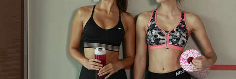 Zwei Frauen stehen an einer Wand und tragen Sport-BHs.