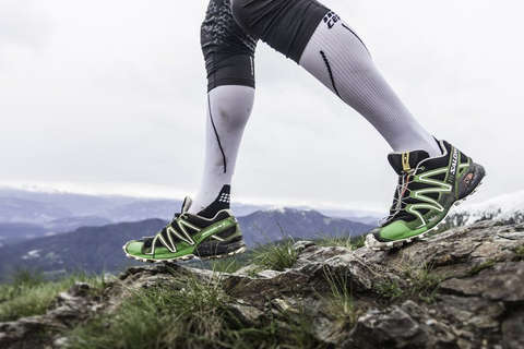 Die Beine eines Trail Runners. Er trägt weiße Kompressionsstrümpfe und schwarz grüne Salomon Trailrunning Schuhe.