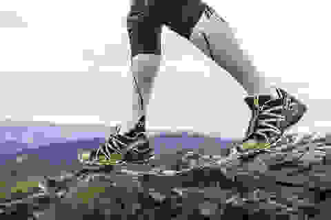 Die Beine eines Trail Runners. Er trägt weiße Kompressionsstrümpfe und schwarz grüne Salomon Trailrunning Schuhe.
