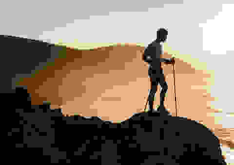 Ein Trailrunner steht mit Trailrunning Stöcken in der Hand während eines Sonnenuntergangs auf einer Anhöhe.