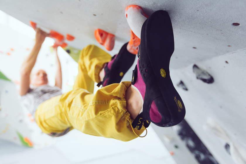 Eine Bouldererin mit gelber Kletterhose hängt an der Kletterwand