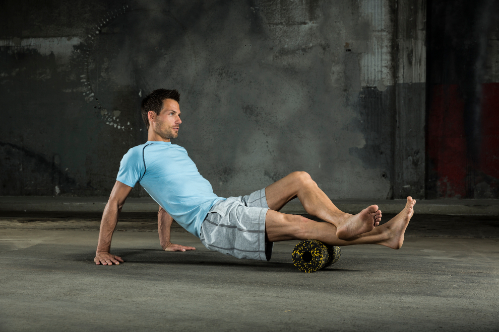 Ein Mann massiert mit einer Faszienrolle seine Wade.