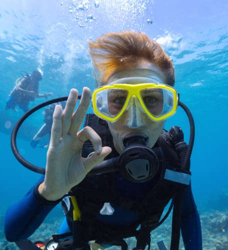 Eine Taucherin in Neoprenanzug macht mit den Händen das Zeichen für "Okay" unter Wasser.