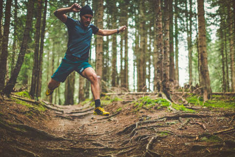 Ein Trailrunner springt über Baumwurzeln die auf einem Waldweg vorhanden sind.