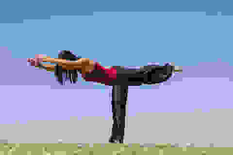 Eine Frau in schwarzer Hose und rotem Oberteil macht eine Yoga Übung unter freiem Himmel.