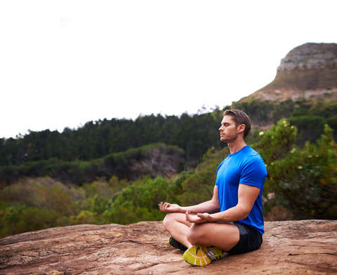 Ein Mann sitzt in der Natur im Lotussitz und meditiert.